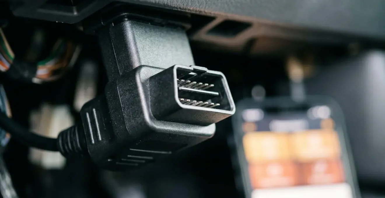 Close-up macro shot of compact Bluetooth OBD2 diagnostic adapter with smartphone displaying live vehicle data